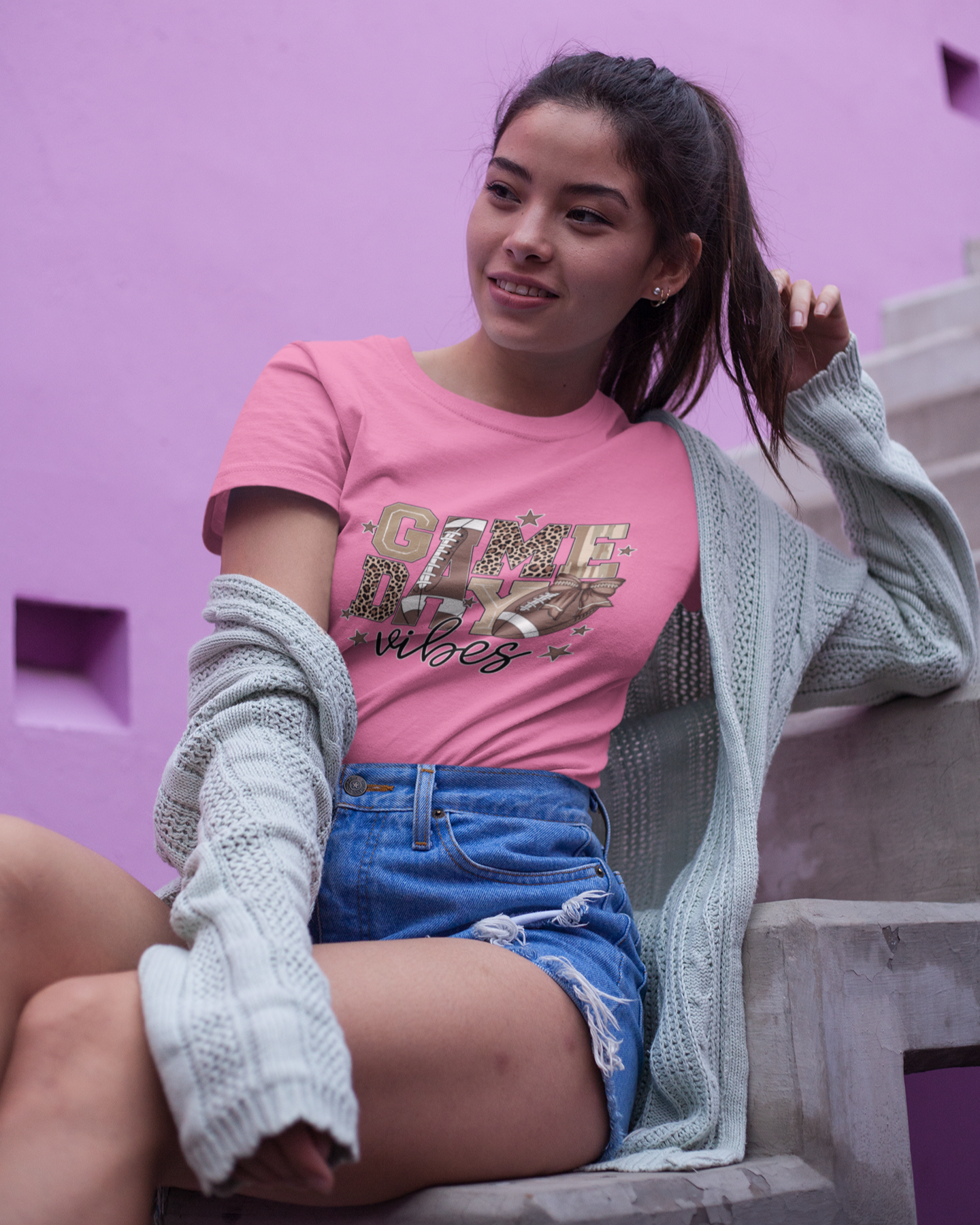Woman wearing a pink t-shirt with text, sitting against a pink wall.