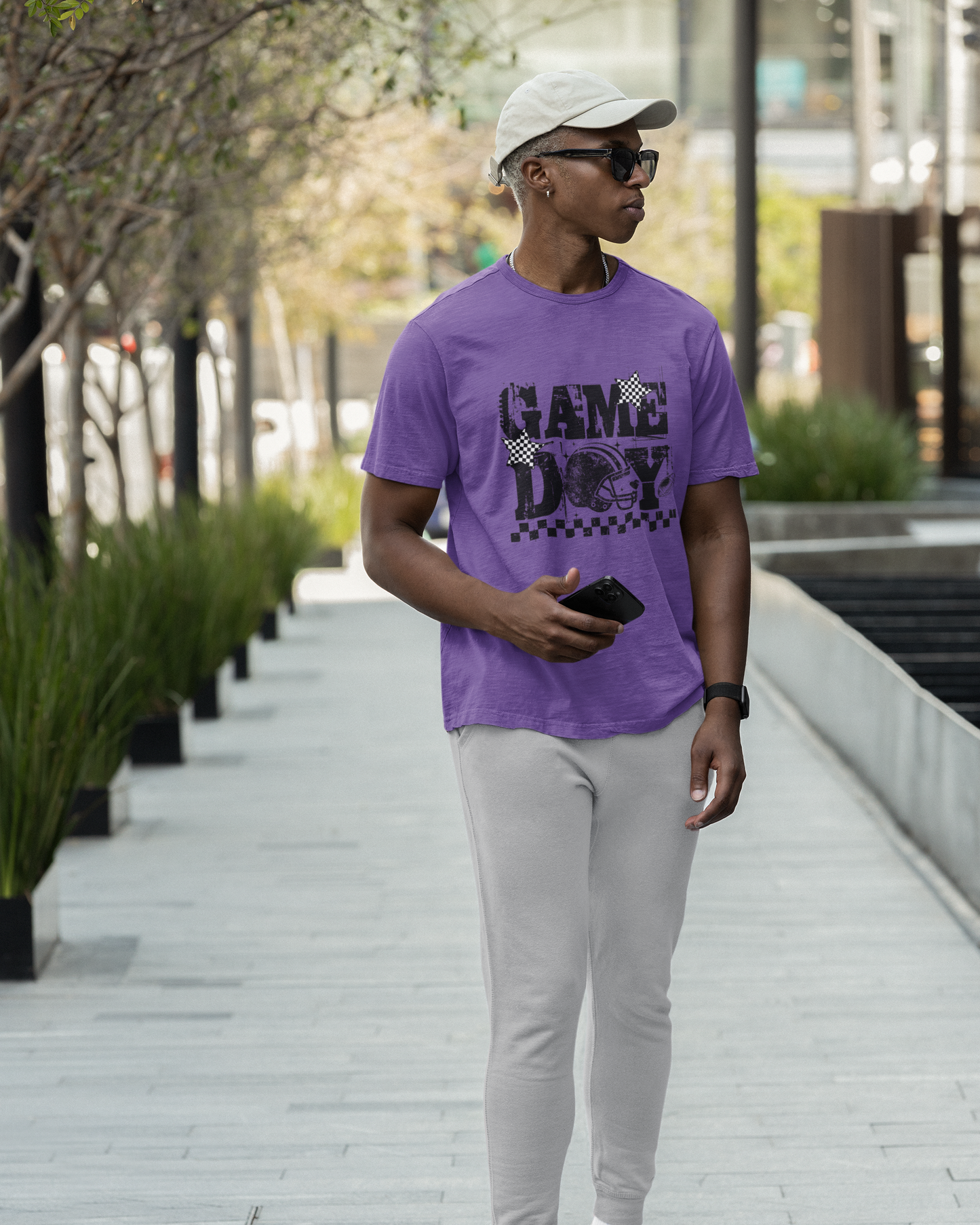 Person wearing a purple 'GAME DAY' t-shirt, gray pants, and black sandals walking outdoors.