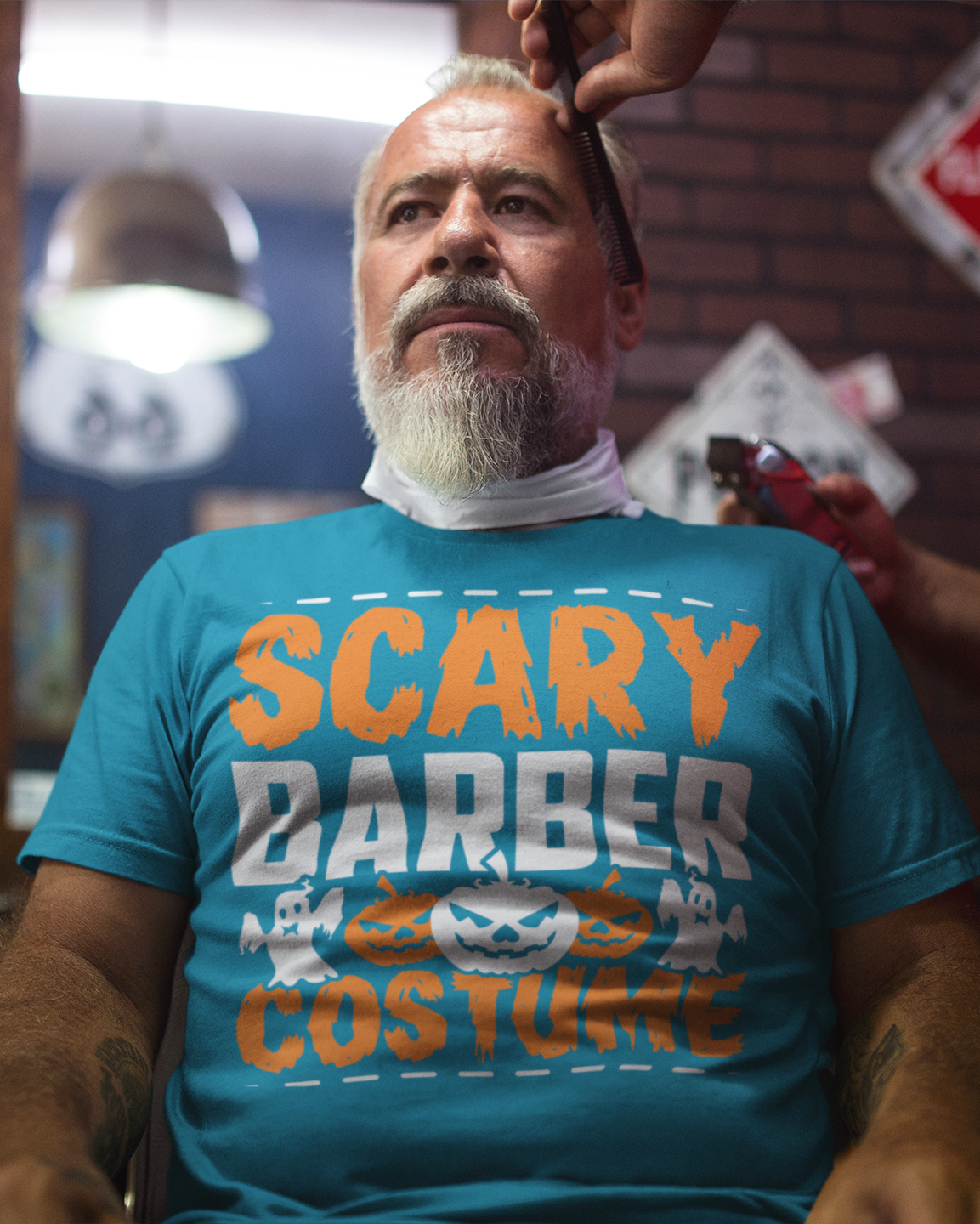 Man getting a haircut wearing a blue t-shirt with 'Scary Barber Costume' text in a barbershop.