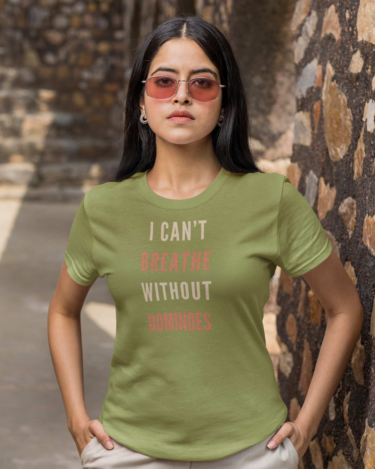 Woman wearing a green t-shirt with text standing against a stone wall.
