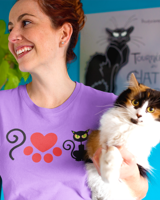 Woman wearing a purple t-shirt with a cat design, holding a calico cat against a blue wall.