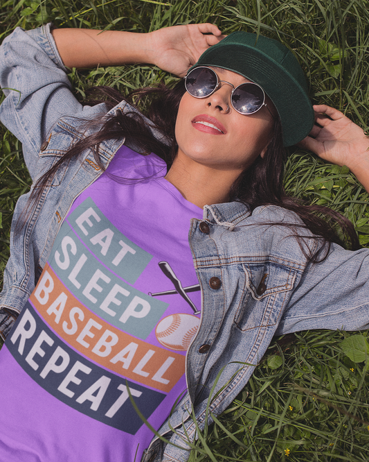 Woman wearing a purple shirt with 'Eat Sleep Baseball Repeat' text, lying on grass.