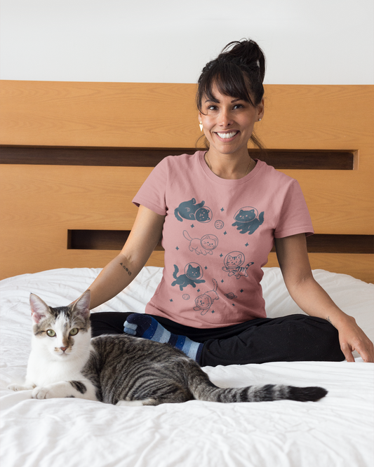 Woman wearing a pink t-shirt with cat designs sitting on a bed with a cat beside her.