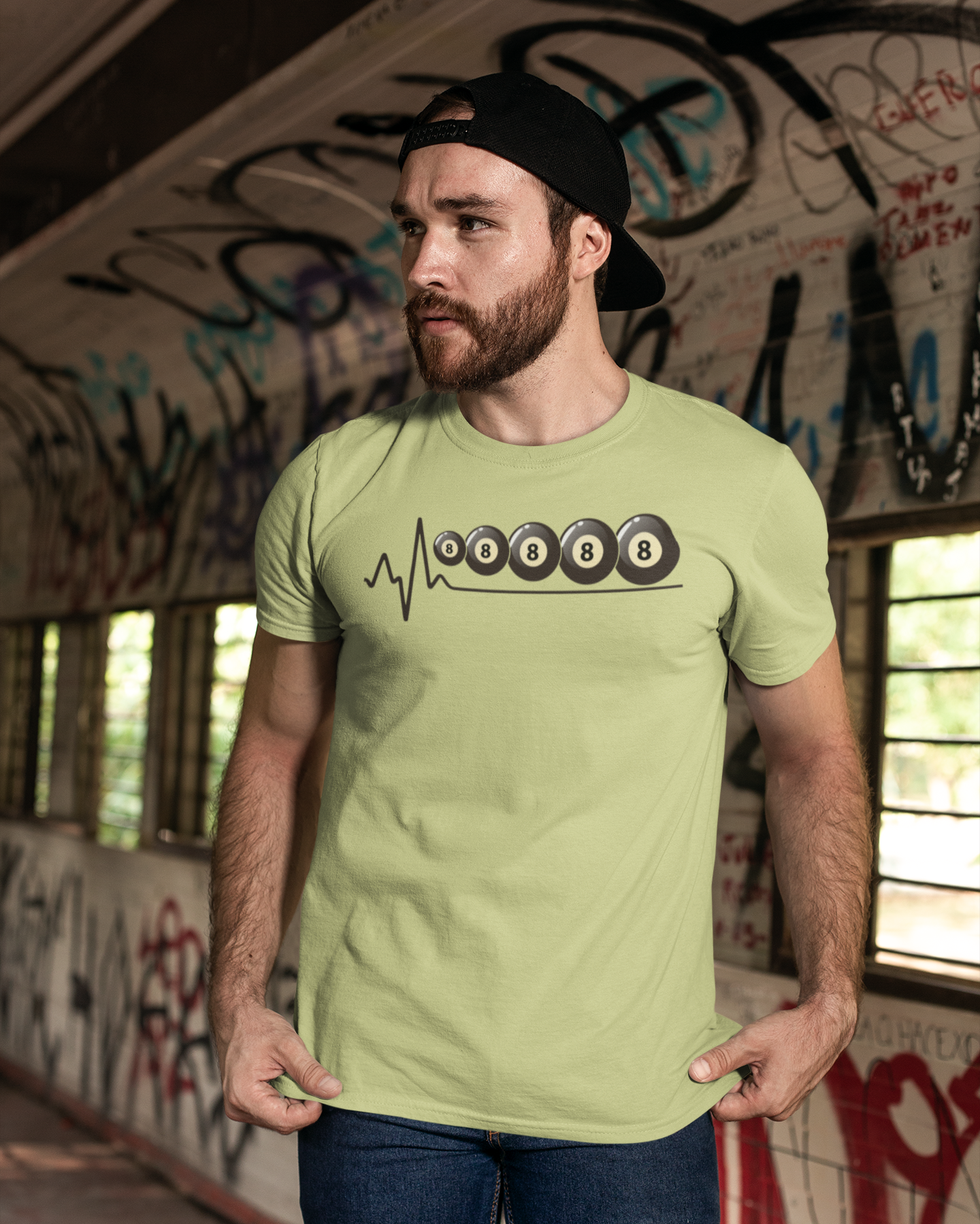 Man wearing a light green t-shirt with a logo in an urban setting with graffiti.