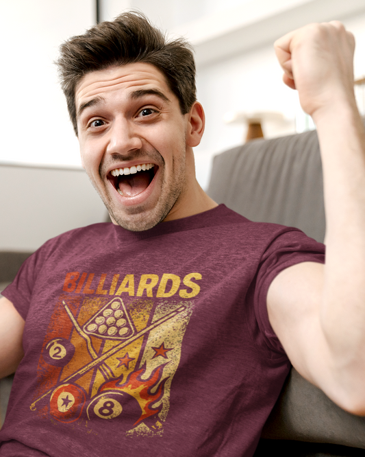 Man sitting on a couch holding a phone, wearing a maroon t-shirt with billiards design.