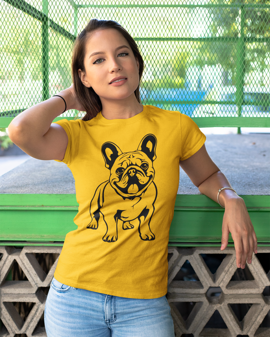 Woman wearing a yellow t-shirt with a black dog graphic, standing against a green metal fence.