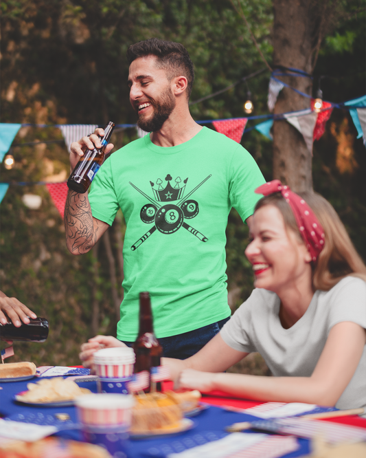 Man in a green t-shirt with a graphic design, holding a beer bottle, standing next to a woman at an outdoor table with food and drinks.