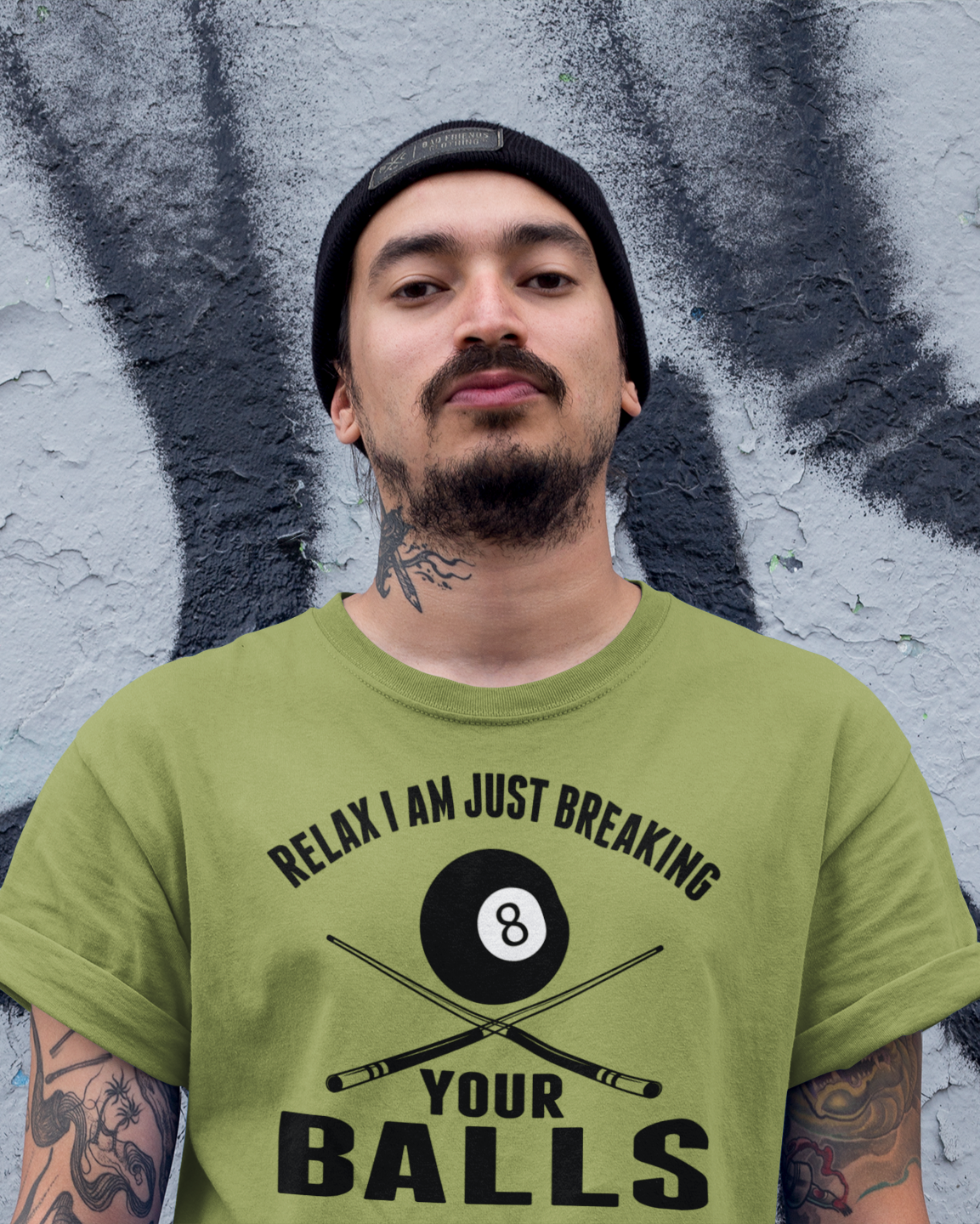 Person wearing a green t-shirt with a graphic and text in front of a graffiti-covered wall.